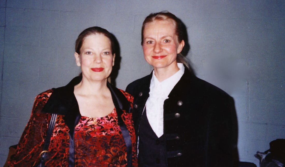 Two women standing next to each other in front of a gray background.