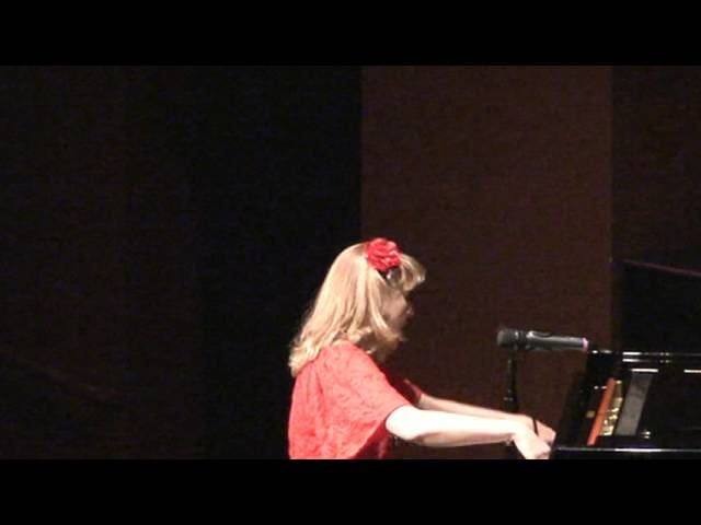 A woman in red shirt playing piano on stage.